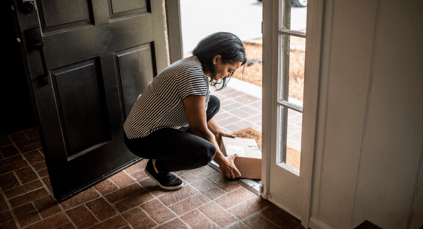 customer benefitting from supply chain visibility by picking up a package at her doorstep that was delivered on time